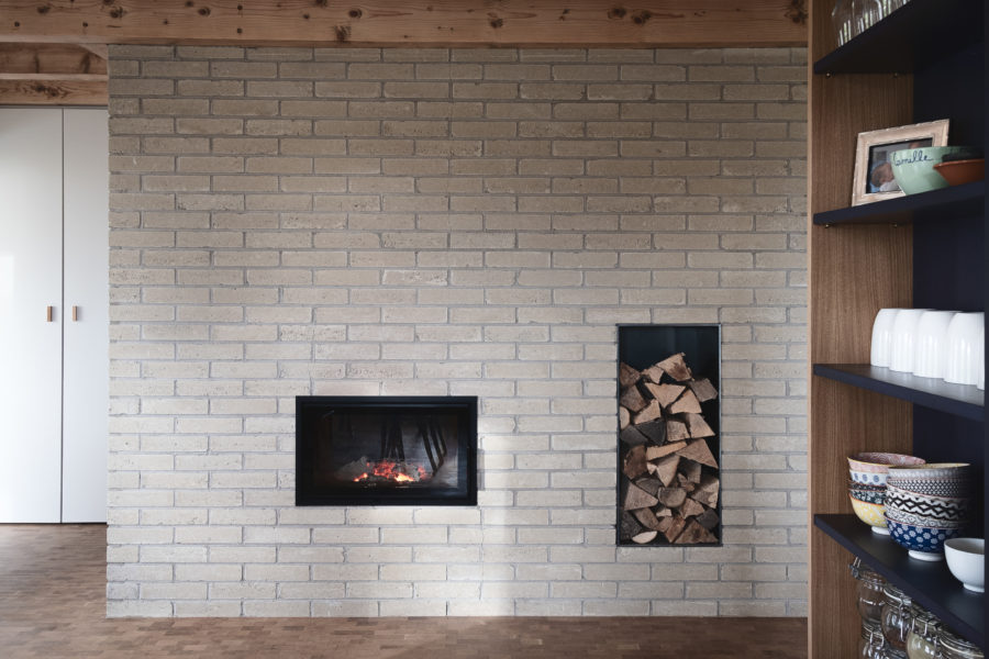 Vue de face sur le mur intérieur en briques avec le poêle a bois et une étagère à droite.